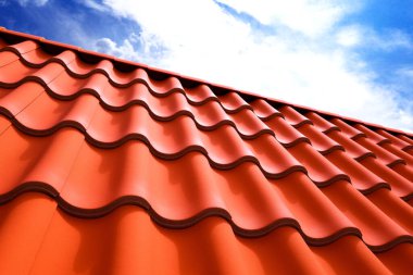Detaylı dokuya ve terracotta çatı kiremitlerinin canlı kırmızı rengine odaklanan çekici bir manzara, karşıt bir mavi gökyüzü arka planı ve yumuşak bulutlar.