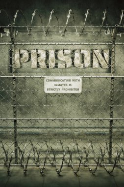 Yüksek güvenlikli bir hapishane sınırını simgeleyen net bir görüntü. Etrafı tel örgüler ve dikenli tellerle çevrili. Katı gözetim ve hapsi simgeliyor..