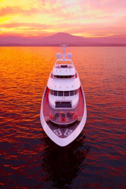 Şatafatlı bir yatın büyüleyici görüntüsü sakin sularda yüzerken çarpıcı bir günbatımının altında, berrak turuncu ve mor renkler okyanusa yansıyor..