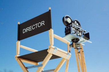 Bu ilgi çekici sahne, 'DIRECTOR' ile kazınmış klasik bir film kamerası ile birlikte, canlı bir mavi gökyüzünün zeminine karşı kurulmuş klasik bir yönetmen koltuğu yakalar..