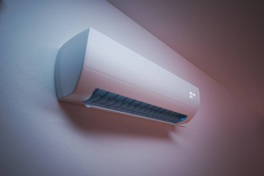 Bu görüntüde şık, modern bir klima ünitesi var. Renkli bir duvara ustalıkla monte edilmiş. Son teknoloji klima kontrol teknolojisini simgeliyor..