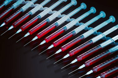 Bu resim, her biri kırmızı sıvıyla dolu bir dizi tıbbi şırınga sergiliyor, titizlikle siyah bir zemine dizilmiş, klinik önemlerini vurguluyor..