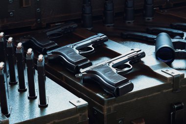 Dergiler, dürbünler ve mermilerle dolu ahşap bir çantada geniş bir dizi tabanca sergilenerek, taktiksel ve koleksiyonluk ateşli silahlardaki çeşitliliği vurguluyor..