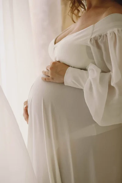 穿着时髦白色衣服的孕妇抱着肚子在工作室里摆姿势 孕妇腹部的近照 典型的母性概念 — 图库照片