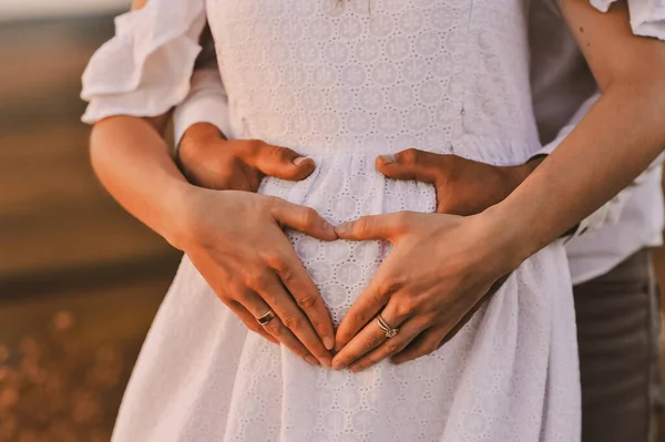 穿着白衣的孕妇和她的丈夫手拉手在怀孕的肚子上 爱的概念 家庭观念快乐生儿育女的概念 — 图库照片