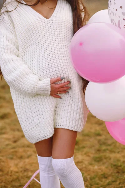 穿着白色针织衫的孕妇一只手拿着粉色和白色气球 另一只手拿着怀孕的肚子 性别党 这是一个女孩 男孩或女孩 — 图库照片