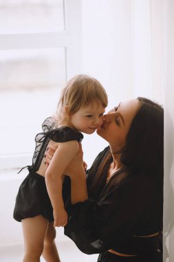 Mutlu anne çocuğunu kucaklıyor ve pencerenin yanında öpüşüyor. Neşeli çocukluk ve aile kavramı. Güzel anne ve bebeği. Metin için alanı kopyala