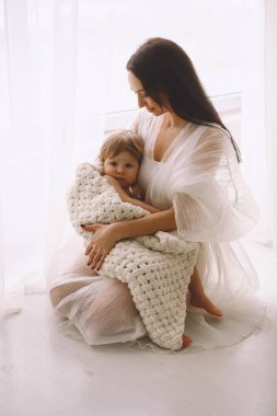 Beyaz elbiseli anne pencerenin yanında oturuyor ve küçük kızını kollarına alıyor. Ebeveyn koruması, bakım, sevgi, çocuk ve bebek sağlığı. Mutlu çocukluk kavramı. Metin için alanı kopyala