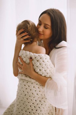 Mutlu anne, küçük kızına evde sarılıyor. Evde örgü örülü battaniyeye sarılı küçük bir kız. Ebeveyn koruması, bakım ve sevgi. Anne ve kızı.