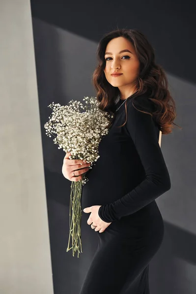 Elinde bir buket çigila tutan ve gülümseyen siyah elbiseli esmer kadının stüdyo portresi. Mutlu annelik ve ebeveynlik kavramı.