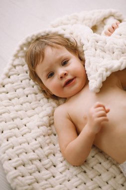 Evde pelüş örgü battaniyeye uzanmış güzel bir kız bebek. Ebeveyn koruması, bakım, sevgi, çocuk ve bebek sağlığı 