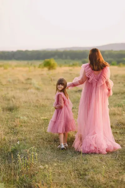 Tulle pembesi elbiseli, annesinin elini tutan ve yaz günbatımında doğada yürüyen güzel bir kızın portresi. Anne ve kızı. Mutlu çocukluk kavramı. Fotoshootin