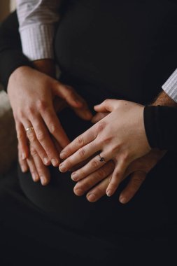 Hamile kadın ve kocasının, elleri hamile karnında kalp şeklini alan fotoğraflarını çek. Yeni bebek bekleyen bir kadın. Mutlu annelik ve ebeveynlik kavramı.