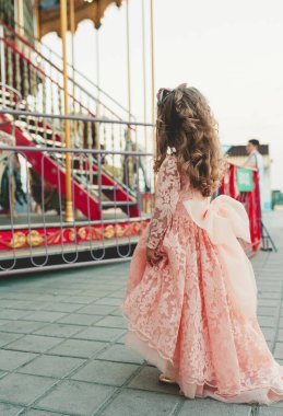 Büyüleyici pembe elbiseli küçük bir kızın atlı karıncaya bakışının arkası. Lunaparktaki bir kız. Mutlu çocukluk kavramı