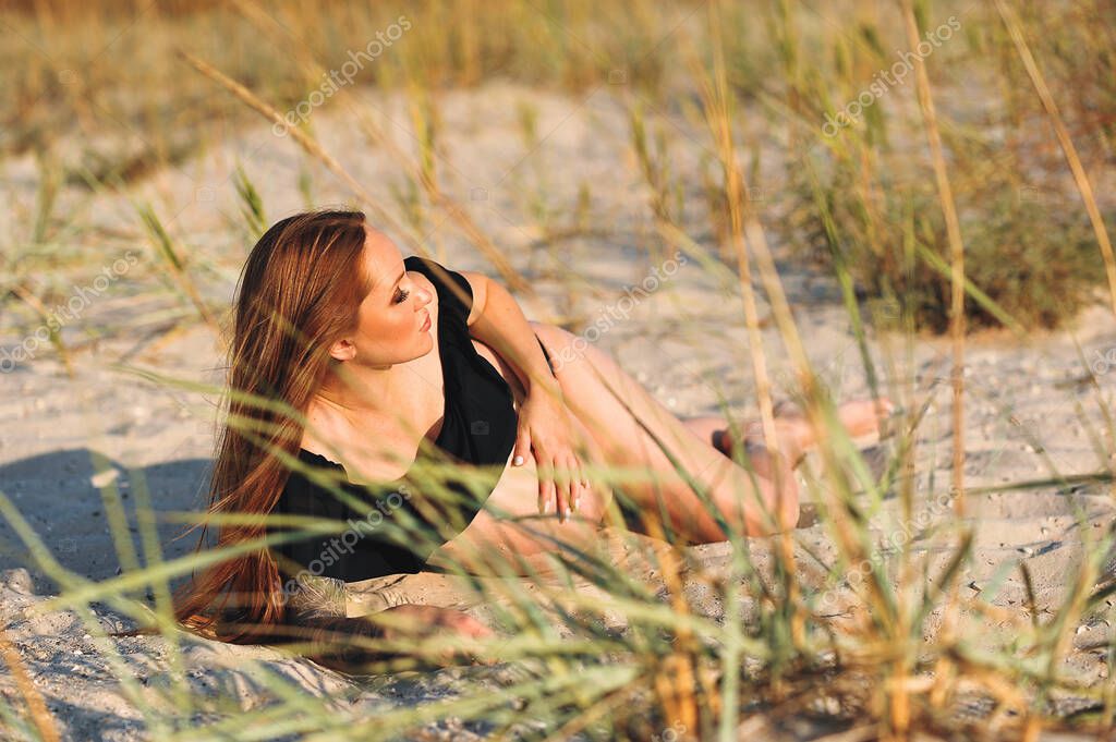 Attractive pregnant woman with red hair in black swimsuit lying on the beach. Stylish Motherhood concept. Relax and recreation