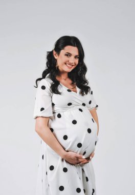 Beyaz benekli elbise giymiş, beyaz arka planda poz veren çekici esmer kadının stüdyo portresi. Güzellik ve moda. Duvar kağıdı ya da baskı dergisi için iyidir. 