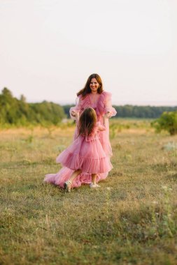 Tüylü pembe elbiseli neşeli anne ve kızı ellerini tutup yazın doğada poz veriyorlar. Sevgi. Aile kavramı. Fotoğraf Çekme