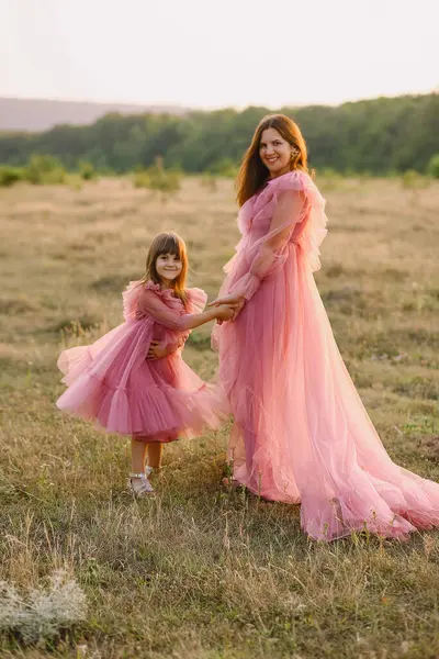 Tulle pembesi elbiseli neşeli anne ve kızı gün batımında doğada poz veriyorlar. Sevgi. Aile kavramı. Fotoğraf Çekme