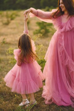 Anne ve kızının yaz aylarında doğada poz veren uzun pembe elbiseleriyle çekilmiş yakın bir fotoğrafı. Tulle pembesi elbiseli, annesinin yardımıyla yazın dans eden güzel küçük kız. Sevgi. Aile kavramı. Fotoğraf Çekme