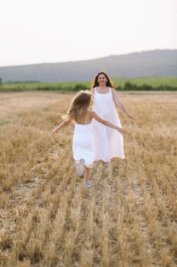 Sahada annesine koşan yazlık elbiseli mutlu bir kız. Mutlu çocukluk kavramı. Aile kavramı. Uzayı metin için kopyala. Yaz fotosoplama