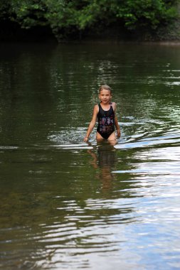 Çocuk gölde ya da nehirde yüzüyor ve eğleniyor. Siyah mayo giymiş güzel bir kız nehirde oynuyor. Uzayı metin için kopyala. Mutlu çocukluk kavramı