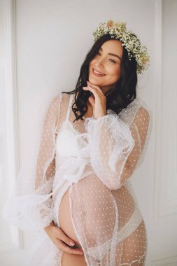 Beyaz puantiyeli hamile kadın portresi ve beyaz çelenk stüdyoda beyaz duvarın yanında poz veriyor. Güzel hamilelik. Mutlu annelik kavramı.