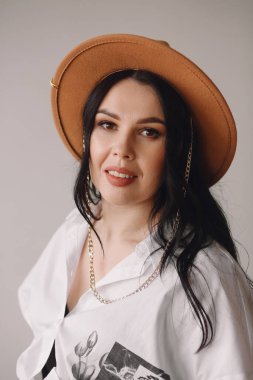 Modern makyajlı, kahverengi fötr şapkalı ve beyaz gömlekli gülümseyen esmer kız portresi. Şık bir kız. Dekoratif kozmetik reklam konsepti