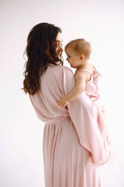 Küçük kızını beyaz arka planda tutan mutlu bir annenin dikiz görüntüsü. Anne ve küçük kızı aynı kıyafetler içinde. Aile görünüşü. Annelik içeriği, anneler günü konsepti. Arka plan