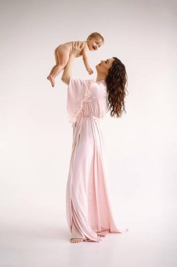 Uçalım! İpek elbiseli, neşeli, genç bir kadın. Küçük kızı ellerinde tutuyor ve ona sevgiyle bakıyor. Stüdyo portresi. Beyaz arka plan. Metin için alanı kopyala