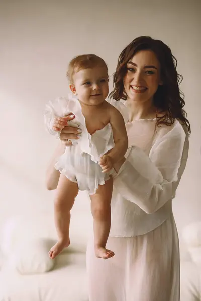 Güzel bir anne ve kızı stüdyoda oynayan havadar beyaz elbiseler giyerler. Mutlu aile eğlenceleri. Yaşam tarzı kavramı.