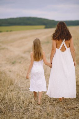 Arka manzara anne ve kızı yaz elbiseleriyle tarlada yürüyor.
