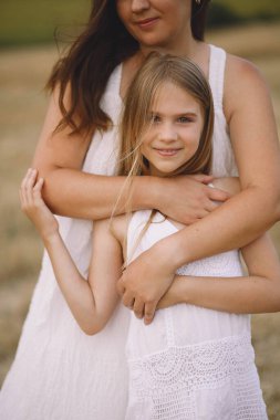 Yazlık elbiseli mutlu anne, tarlada kızını kucaklıyor.