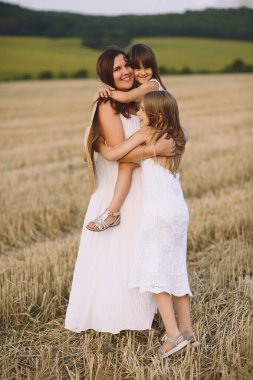Mutlu anne ve kızları yaz elbiseleriyle tarlada kucaklaşıyorlar.