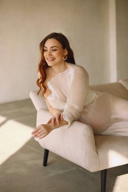 Çekici gülümseyen, şık fildişi elbiseli hamile bir kadının portresi kanepede uzanıyor ve stüdyoda poz veriyor. metin için boşluk kopyala. Güzellik ve moda