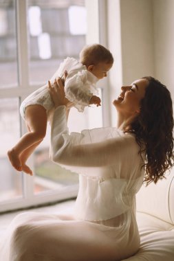 Mutlu anne kanepeye oturur ve küçük kızını kucağına alır. Anne ve kızı aynı elbiseyi giyiyor. Mutlu annelik kavramı. Aile görünüşü
