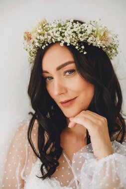 Yeşil gözlü, çelenkli güzel esmer kadın portresi ve beyaz arka planda beyaz peignoir. Güzellik ve moda