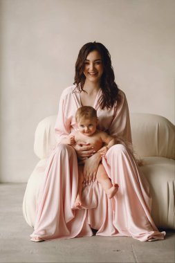 Pembe elbiseli güzel annenin portresi. Çıplak bebeğini kucağında tutuyor ve stüdyoda poz veriyor. Anne ve bebek. Mutlu annelik ve çocukluk kavramı. Kadınlar Günü