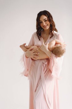 Stüdyoda beyaz arka planda pembe ipek elbiseli güzel bir anne küçük kızıyla oynuyor. Anne ve bebek. Aile kavramı. Aşk konsepti. Kadınlar Günü