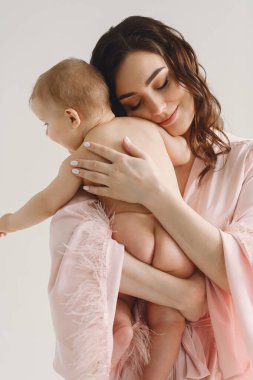 Sevgi dolu bir anne, beyaz arka planda poz verirken çıplak bebeğine sarılıyor. Anne ve kızı. Aile kavramı. Aşk konsepti. Kadınlar Günü