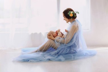 Mavi tül elbiseli, saçı yerde oturan, kucağında bir bebekle gezen sevgili annenin yatay portresi. Anne ve oğlu. Aile kavramı. Metin için boşluk