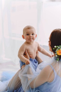 Şık bir anne yerde oturuyor, kucağında bir bebek beşiği var. Anne ve oğlu. Aile kavramı. Mutlu annelik kavramı. Metin için boşluk