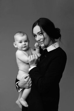 Siyah ceketli ve beyaz gömlekli bir annenin tek renkli stüdyo portresi. Yeni doğmuş bebeğini kucağında tutuyor. Anne ve bebek. Mutlu annelik kavramı