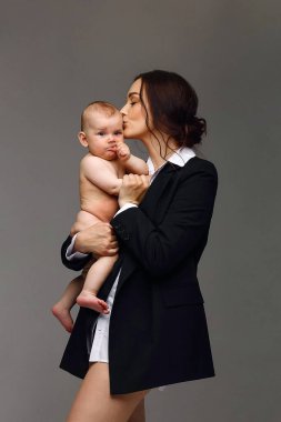 Stüdyo portresi, siyah ceketli ve beyaz gömlekli bir anne ve yeni doğmuş çıplak bebeğinin. Mutlu annelik kavramı. Anne bebeğini öpüyor.