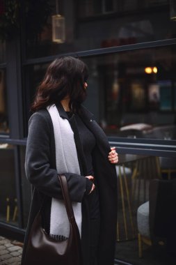 Gri paltolu ve eşarplı şık esmer bir kadının kışın sokaklarda yürüyüşü. Güzellik ve moda. Güzel kıvırcık saç stili. Metin için alanı kopyala