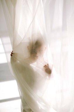 Küçük çocuk evde beyaz bir perdenin arkasında oyun oynuyor ve saklanıyor, eğleniyor. Mutlu çocukluk kavramı