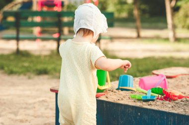 Güzel bir yaz gününde, oyun parkındaki kum havuzunda oynayan küçük bir kızın arka görüntüsü. Çocuklar için açık havada yaratıcı aktiviteler. Mutlu çocukluk, metin için kopyalama alanı