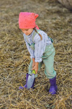 Çiftçi kızın dikey görüntüsü yaz aylarında çiftlikte kürekle saman fırlatıyor. Kırsalda mutlu bir çocukluk. Mutlu yazlar. Kır hayatı, tarım ve kırsal yaşam tarzı.