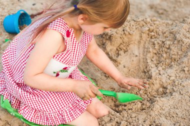 Güzel bir yaz gününde, oyun parkındaki kum havuzunda kürekle oynayan küçük bir kızın yatay görüntüsü. Çocuklar için açık havada yaratıcı aktiviteler. Mutlu yazlar, metin için alanı kopyala
