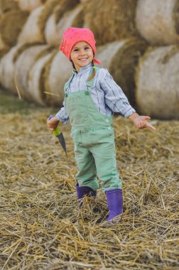 Neşeli çiftçi kız saman balyalarının arka planına kürekle saman atıyor. Kırsalda mutlu bir çocukluk. Mutlu yazlar. Kır hayatı, tarım ve kırsal yaşam tarzı