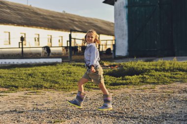 Yazın çiftlikte yürürken gülümseyen çiftçi çocuğun yatay fotoğrafı. Kırsalda mutlu bir çocukluk. Uzayı metin için kopyala. Mutlu yazlar, açık hava yaşam tarzı